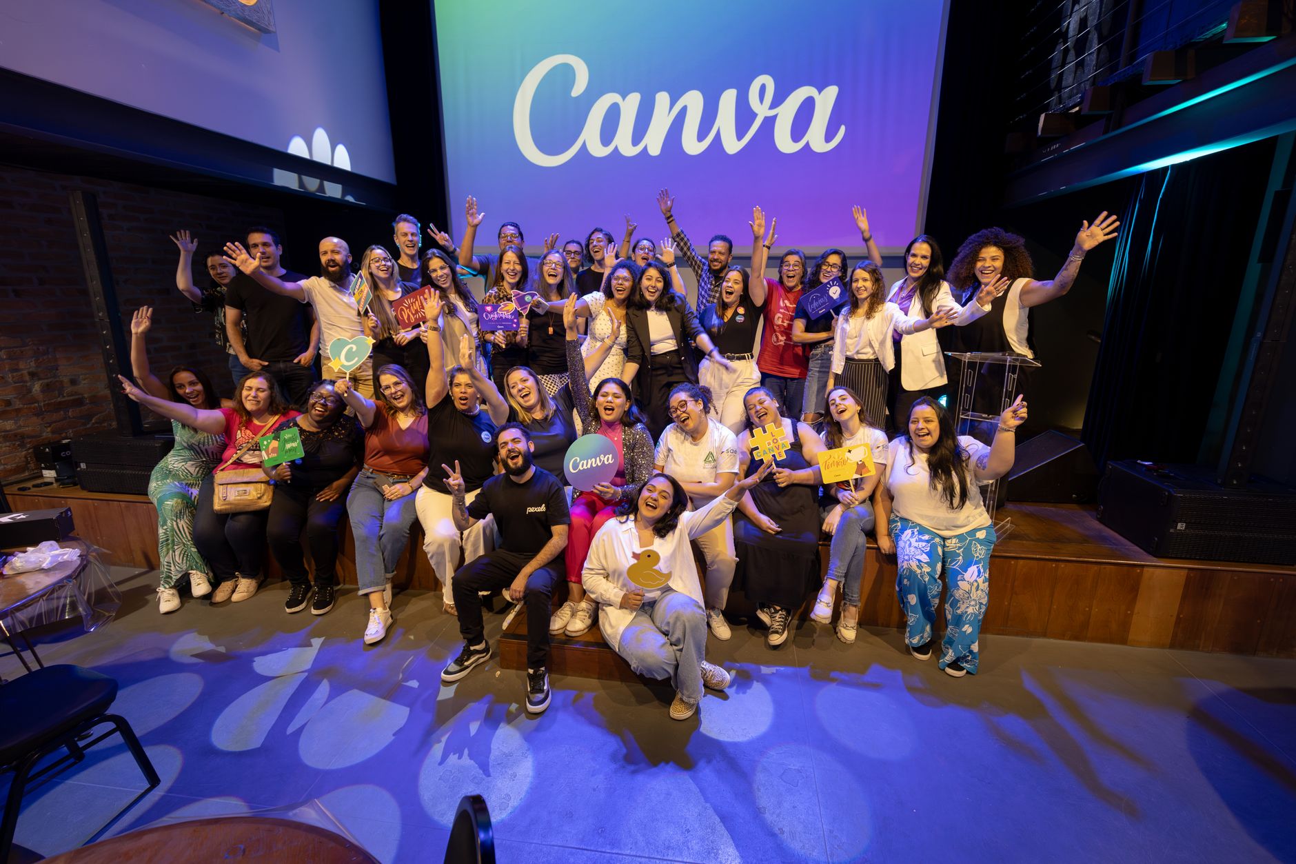 A diverse group of people celebrating on stage indoors, under a bright Canva logo.