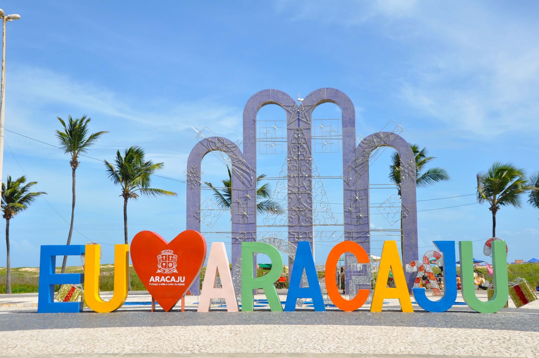 Vibrant EU AMO ARACAJU sign and palm trees under a clear blue sky.
