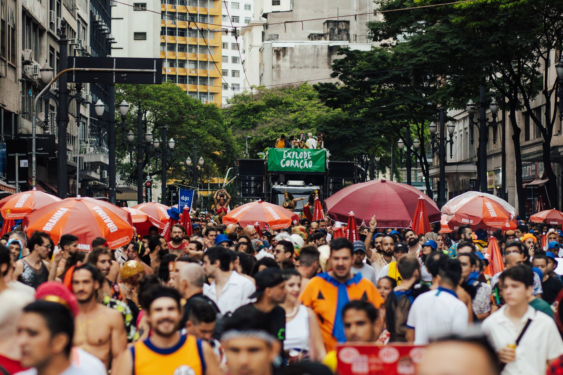 Bustling street parade crowded with diverse people celebrating under colorful umbrellas in a lively city setting.
