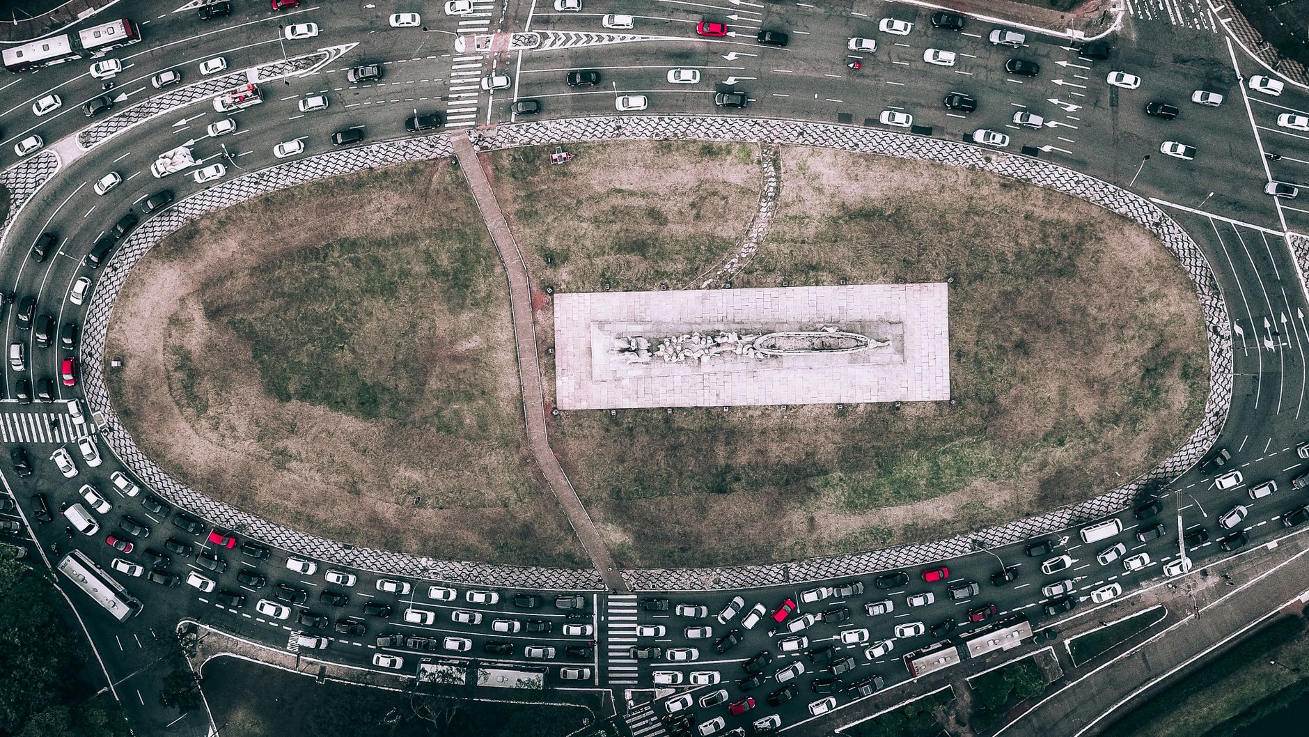 Aerial image of a busy traffic circle surrounding a central monument, showcasing urban life.