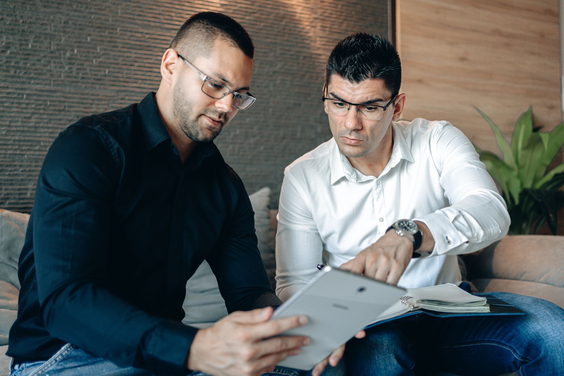 Two men collaborating on a digital tablet indoors, focusing on teamwork.