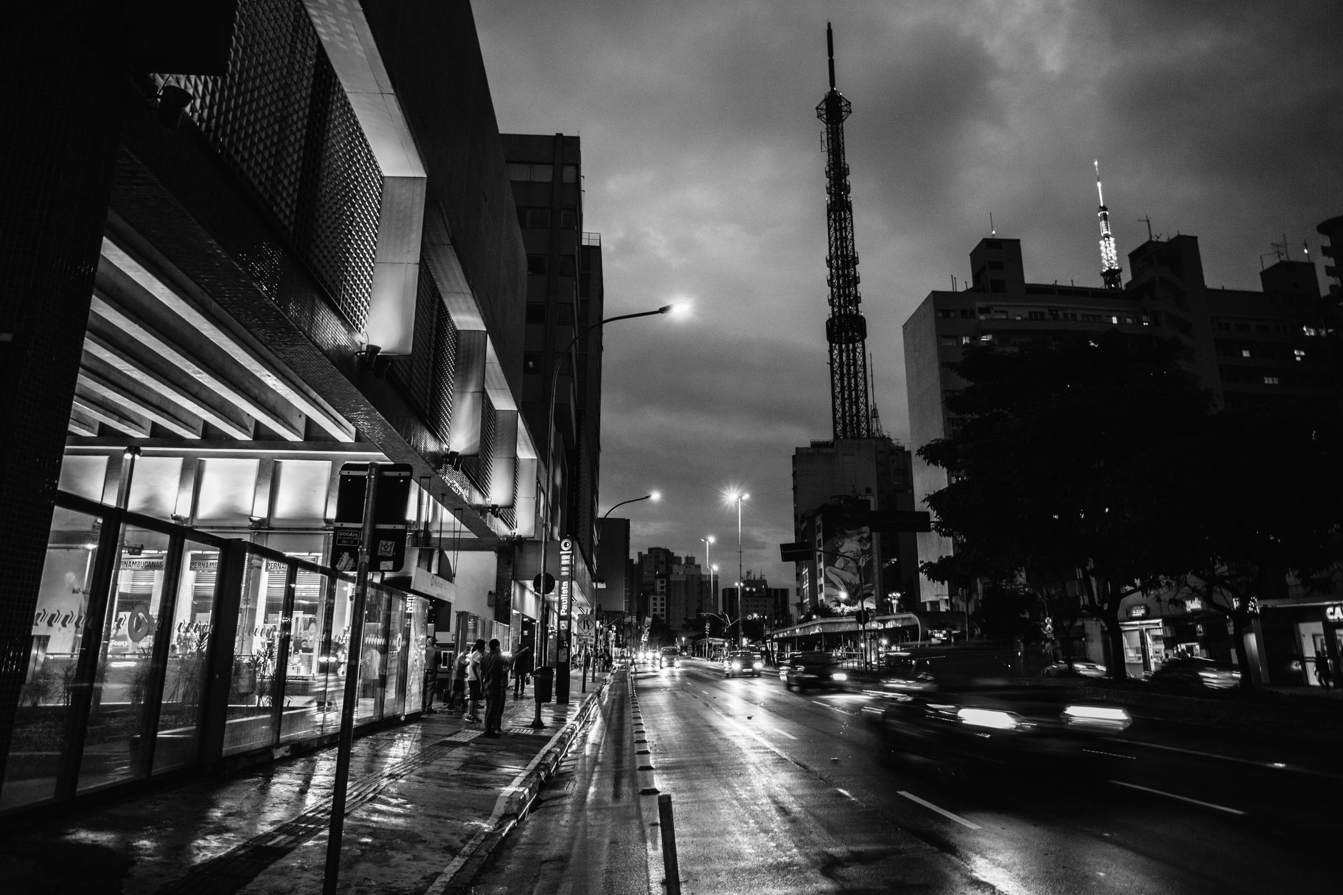 Dramatic black and white cityscape at night featuring a prominent tower and street activity.