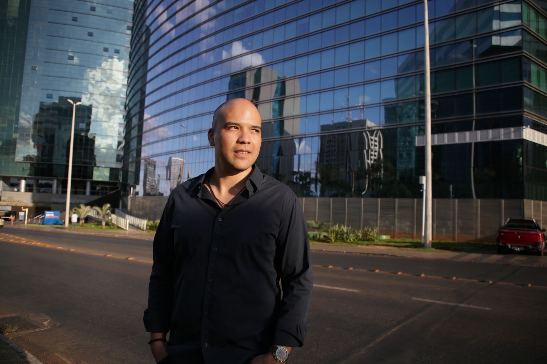 Elegant businessman posing confidently on a modern street in Brasília, with reflective skyscrapers in the background.