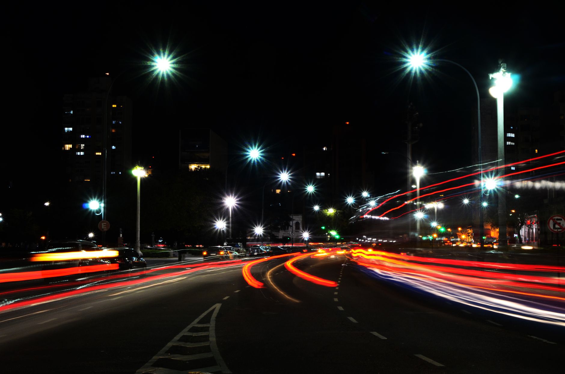 Vibrant urban night scene showcasing car light trails on a bustling city road.