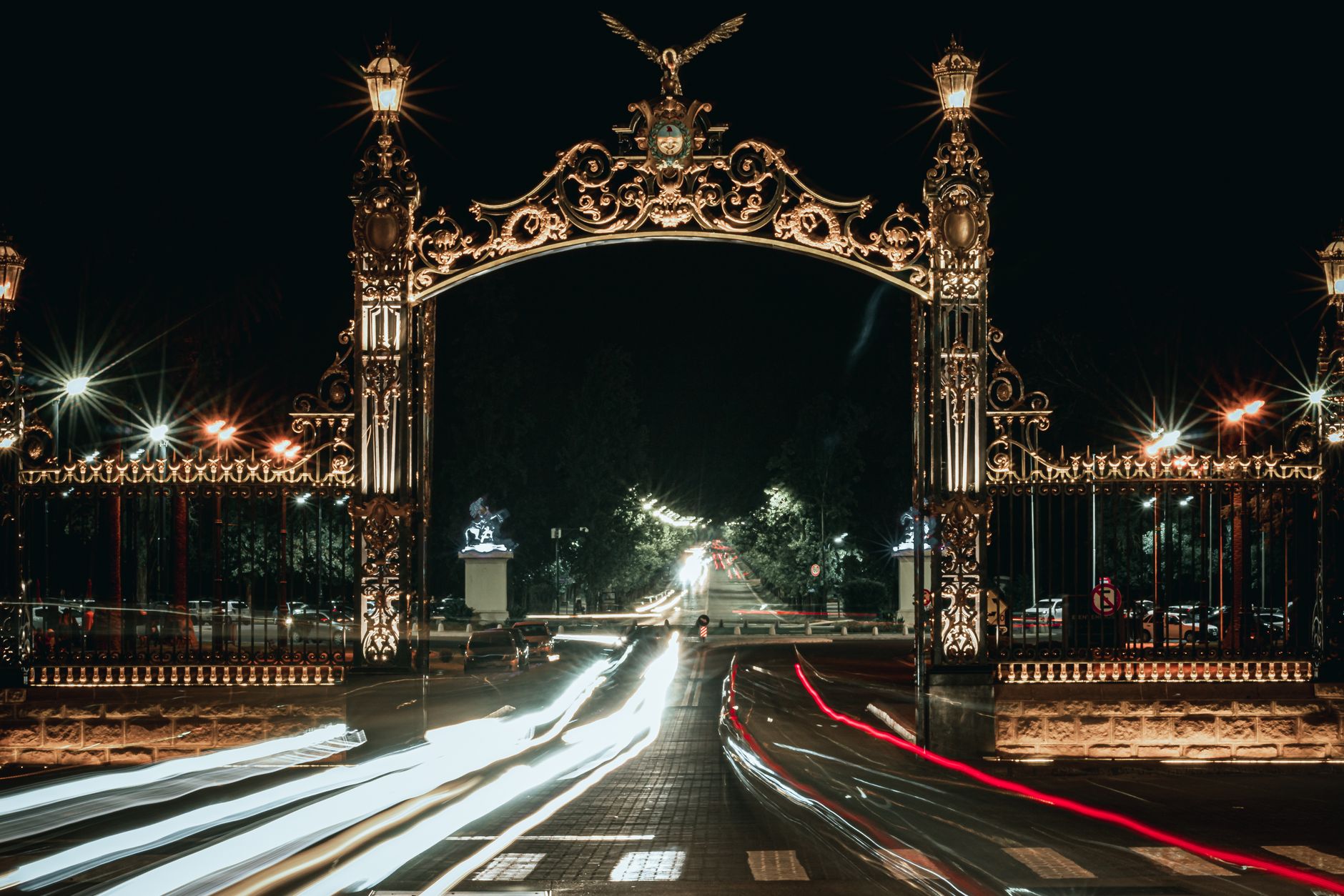 Spectacular night shot of illuminated ornate gate with vibrant light trails and dark sky.