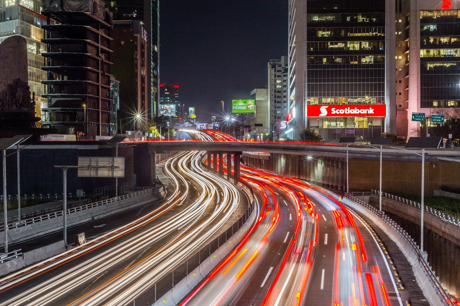 Long-exposure shot of Mexico City's bustling highway at night, with vibrant lights and urban skyline.