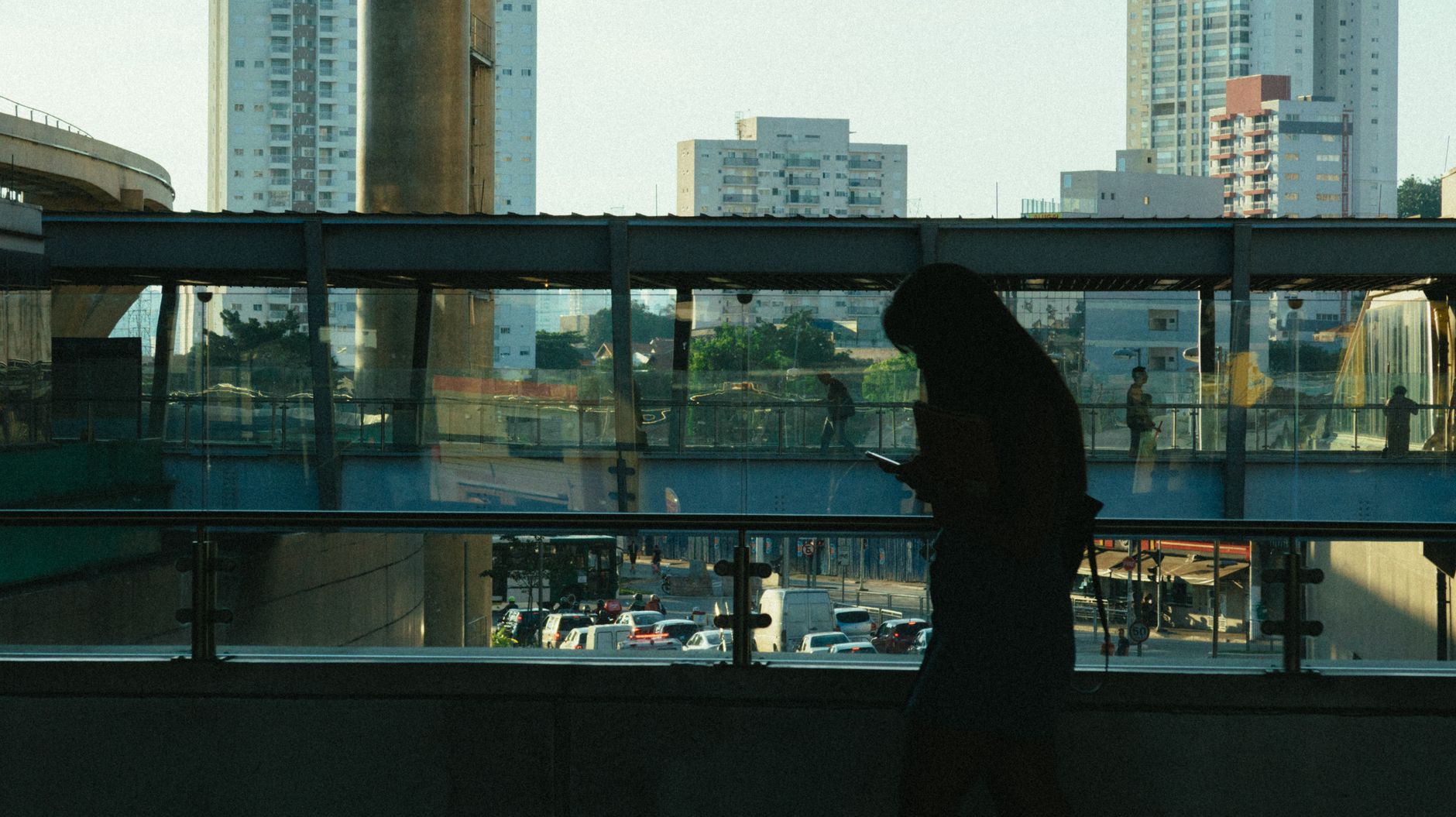 Silhouette of a woman on her phone against a backdrop of an urban landscape with buildings and traffic.
