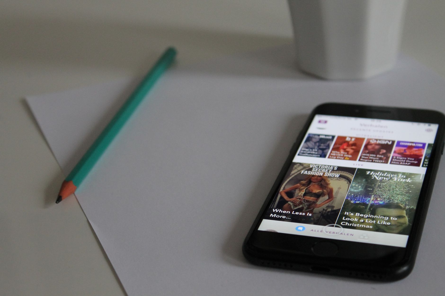 Smartphone displaying news, next to pencil and paper on a desk, showcasing modern technology in a workspace.