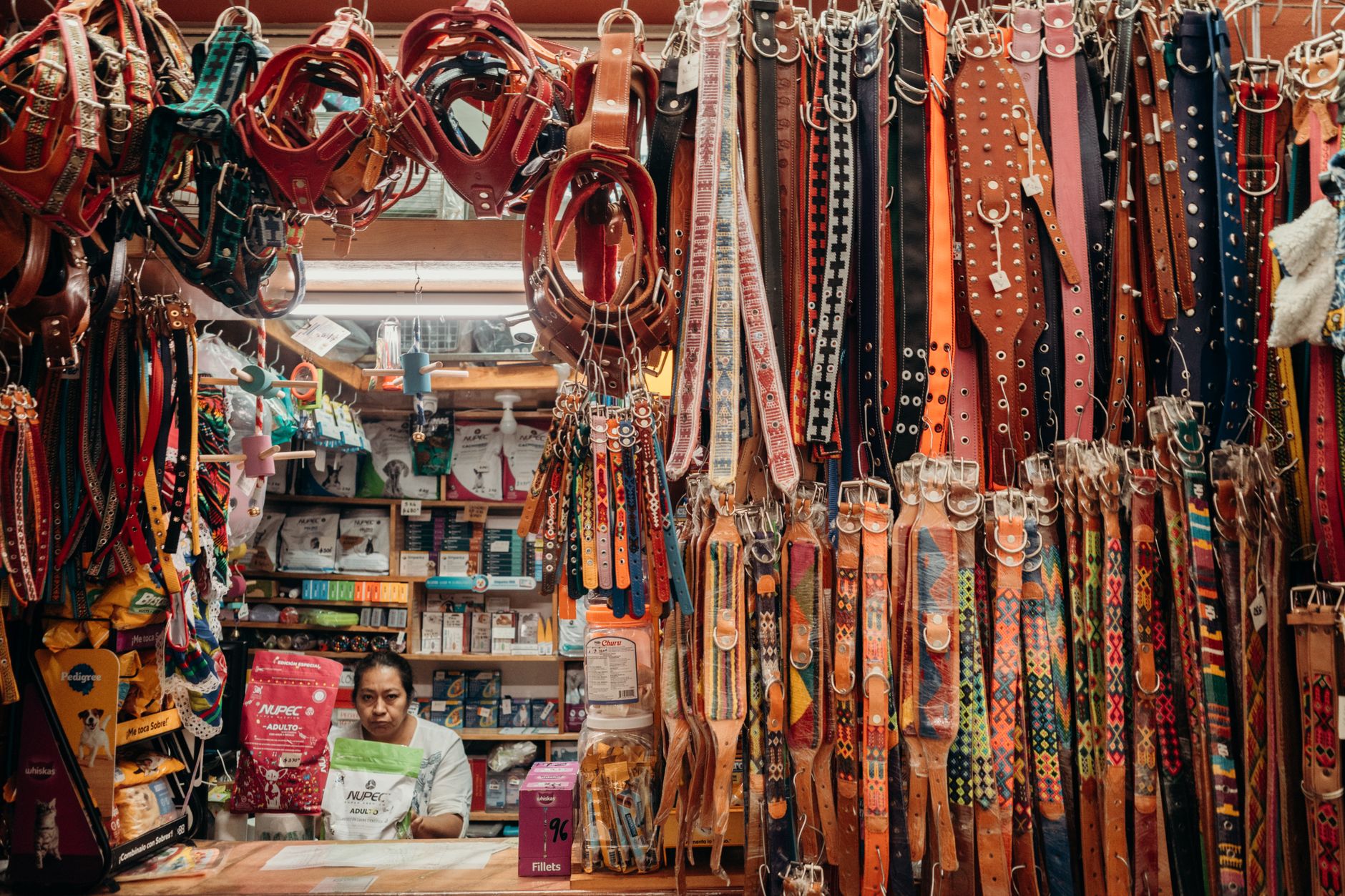 Colorful leather pet collars at an indoor market stall with a vendor.