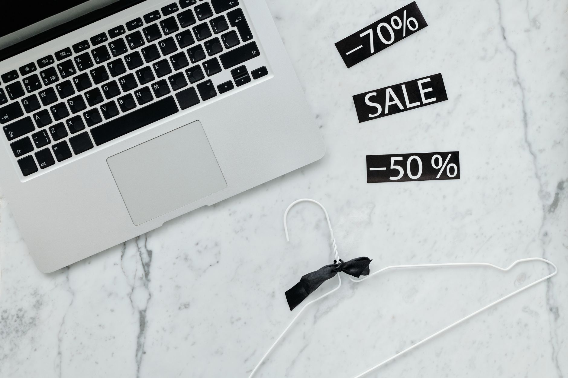 Flat lay of a laptop, hanger, and sale stickers on a marble desk, ideal for Black Friday themes.