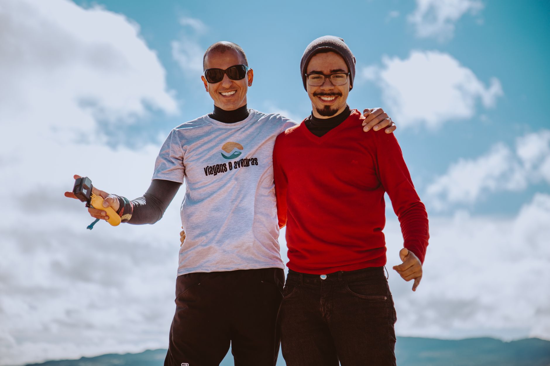 Two cheerful men smiling and posing outdoors under a clear blue sky, exuding friendship and joy.