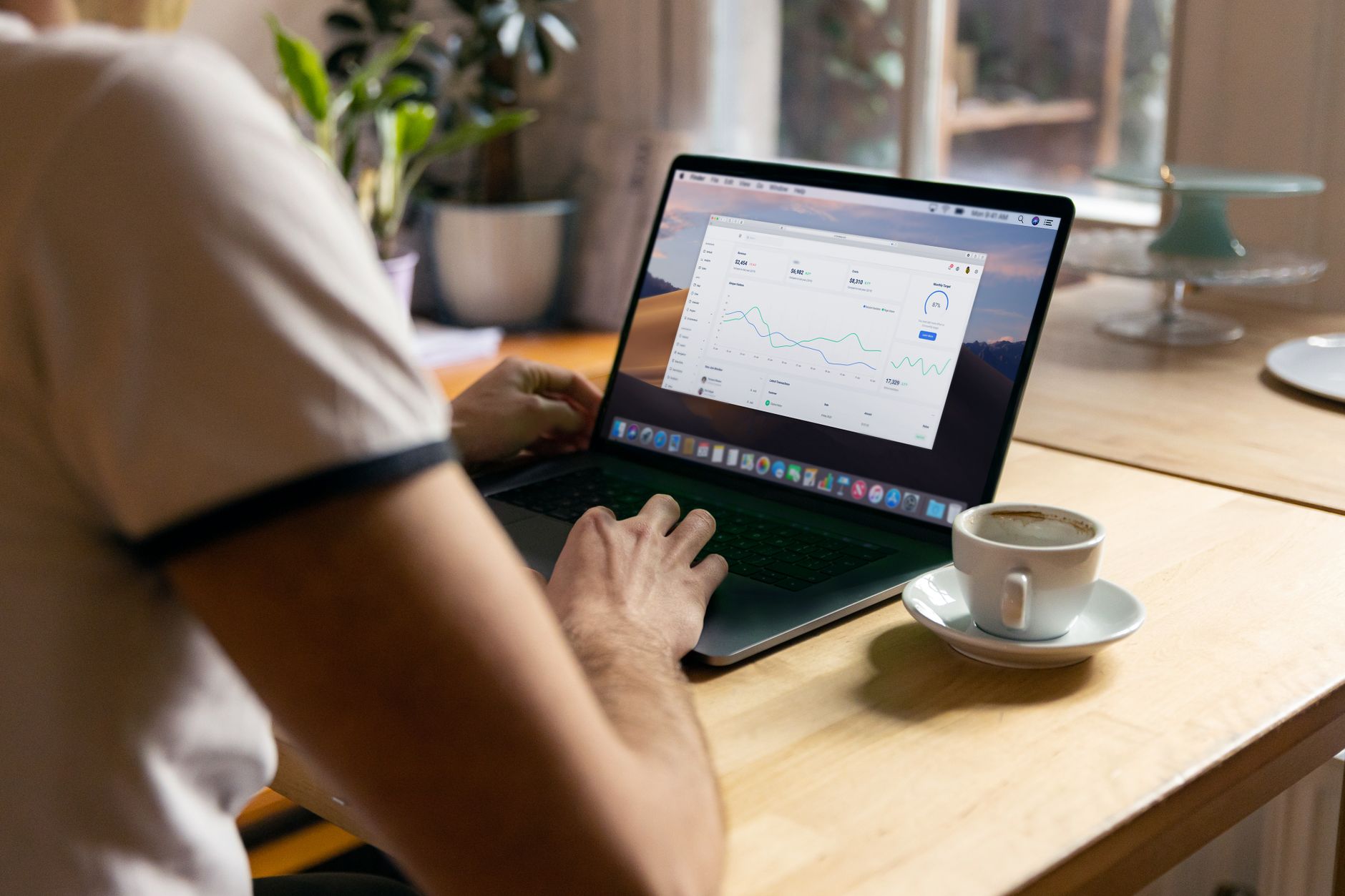 Person working on a laptop with analytics in a cozy home office setting, coffee in hand.