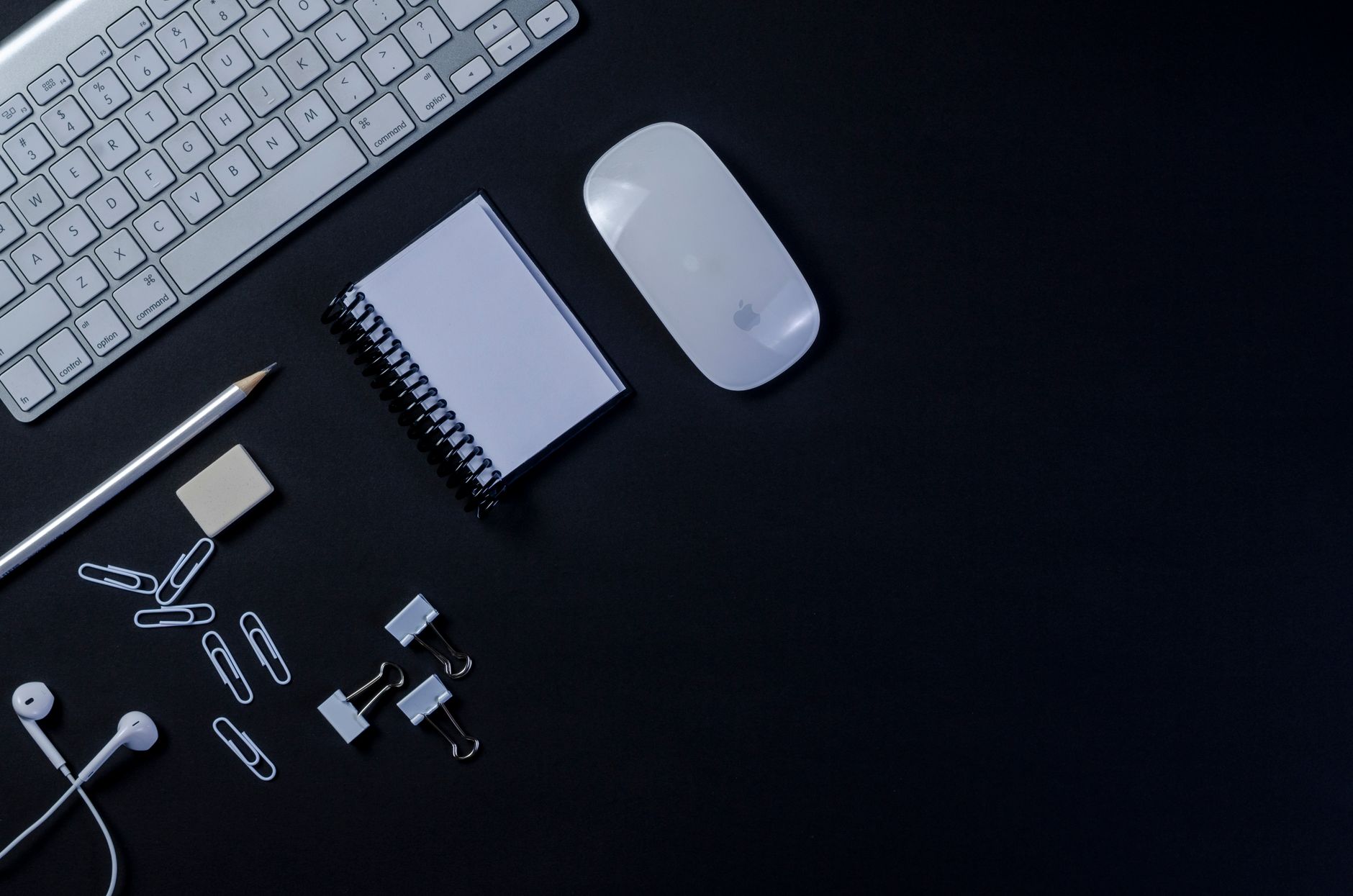 Flat lay of a modern workspace with keyboard, mouse, and stationery on a dark background.