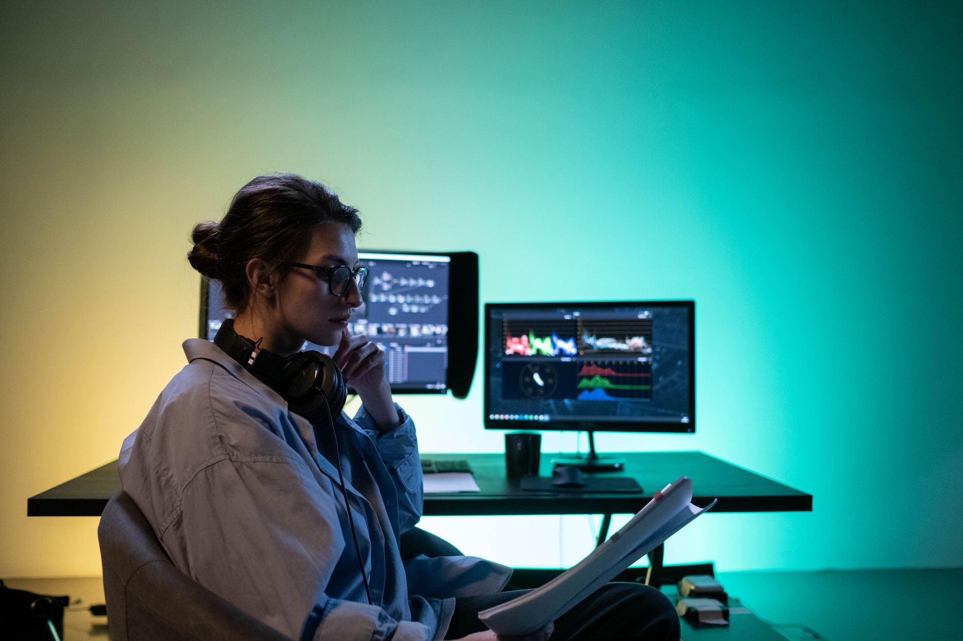 Woman editing video at modern desk setup with dual monitors in an office.