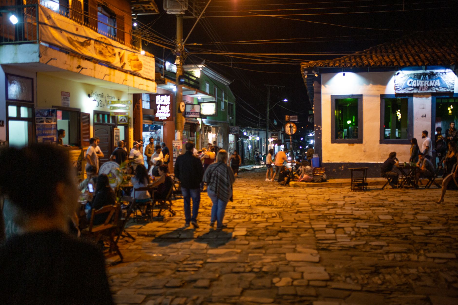 Vibrant nightlife scene with people enjoying cafes and shops on a cobblestone street.