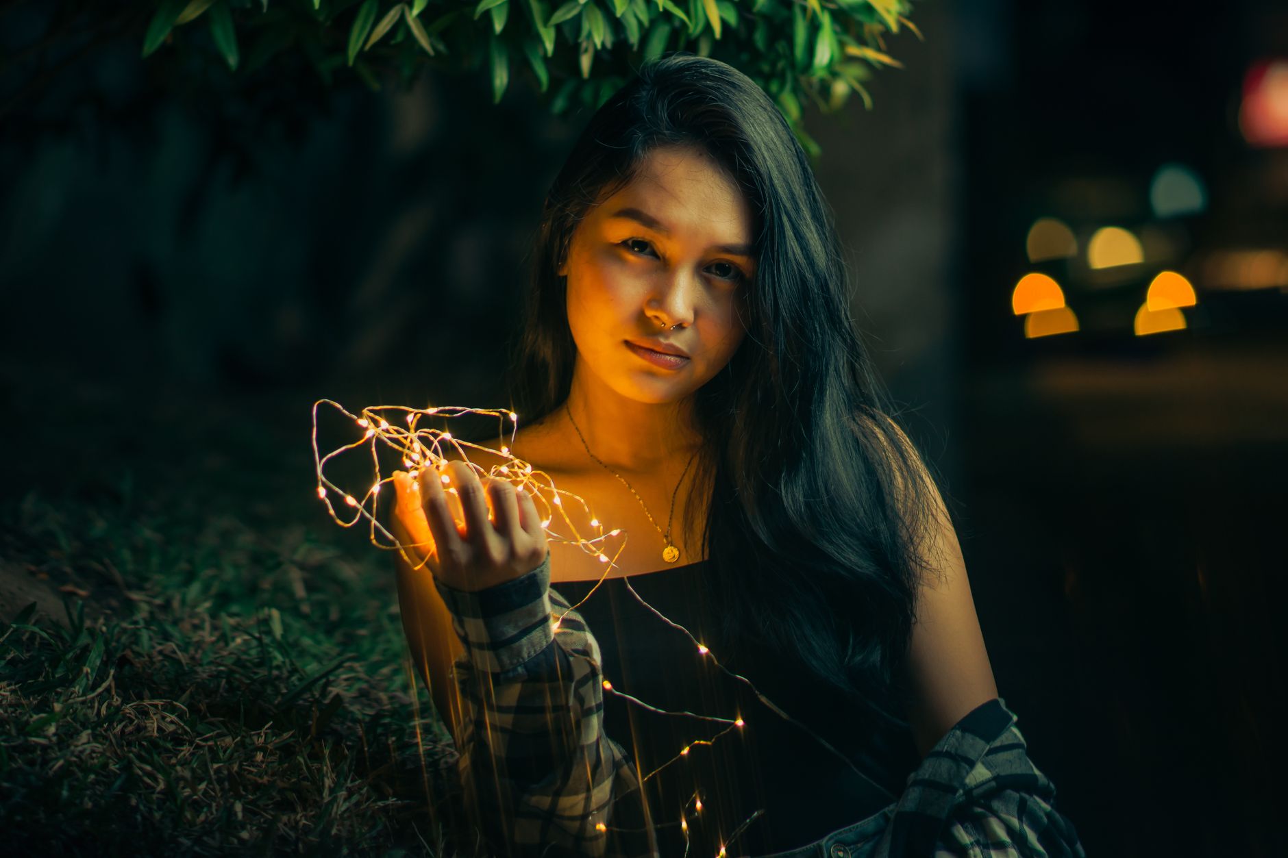 Portrait of a young woman holding string lights, creating a dramatic urban night scene.