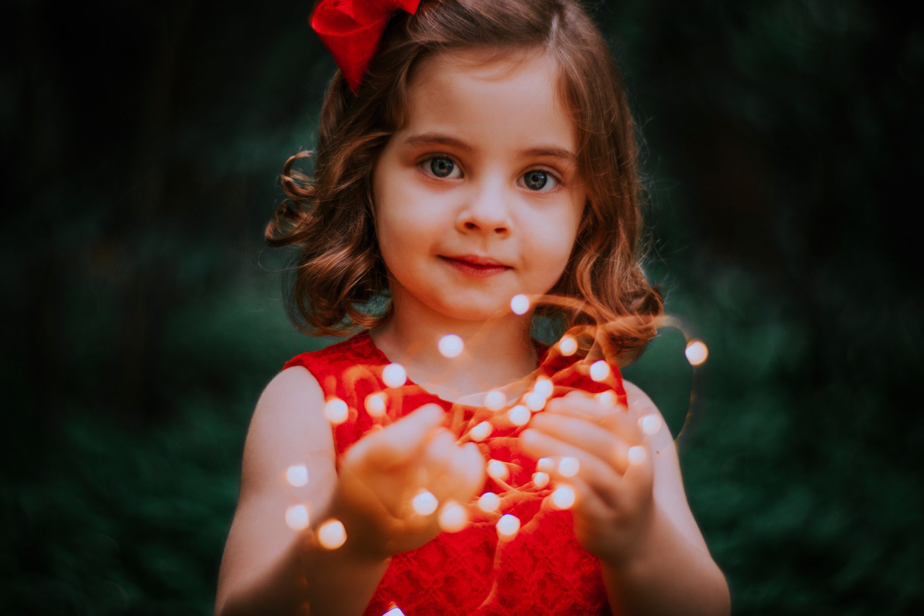 Charming young girl in red dress holding glowing fairy lights, evoking warmth.