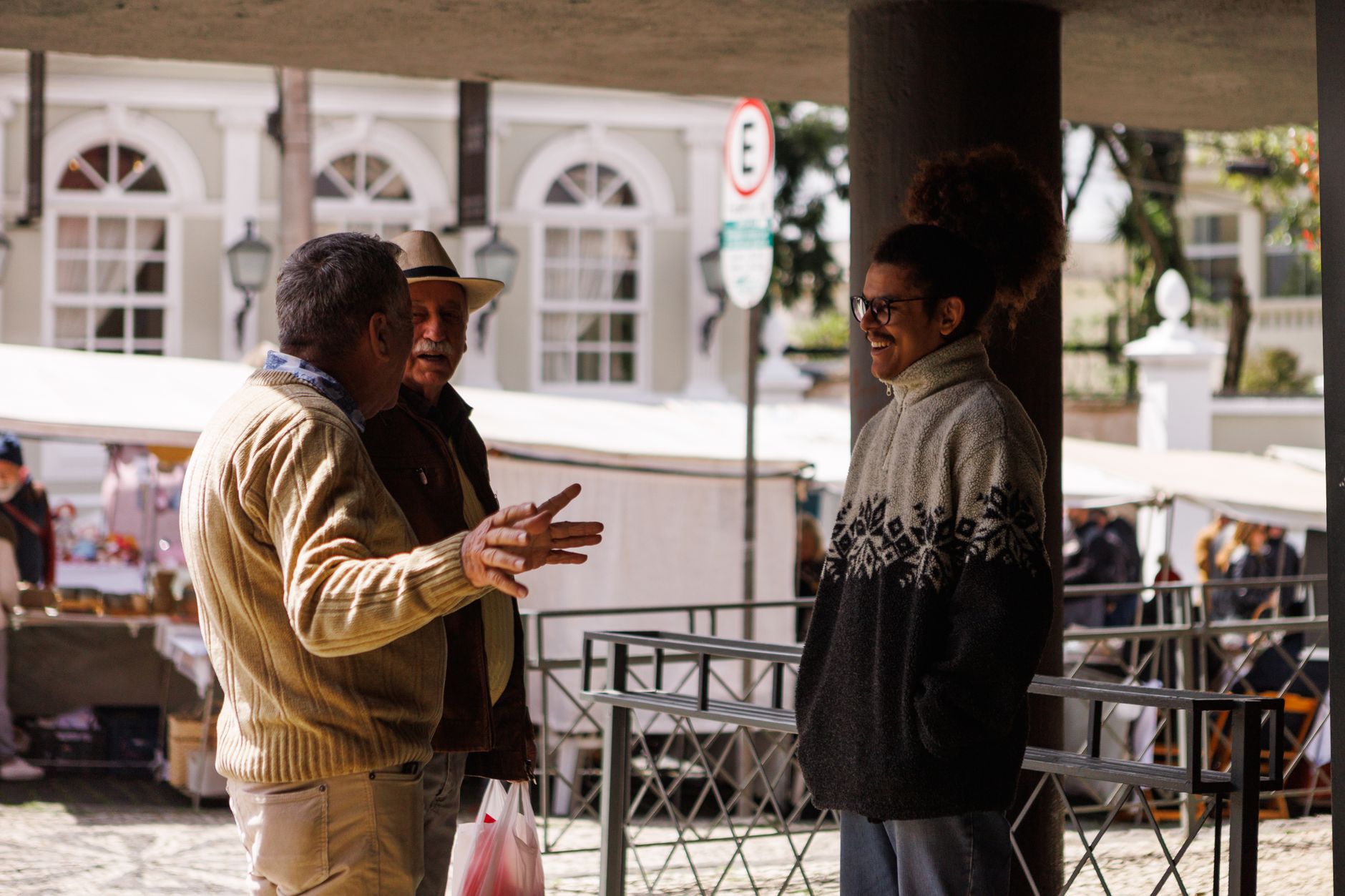 Three men casually chatting in an outdoor market in Curitiba, Brazil, captured during a sunny day.