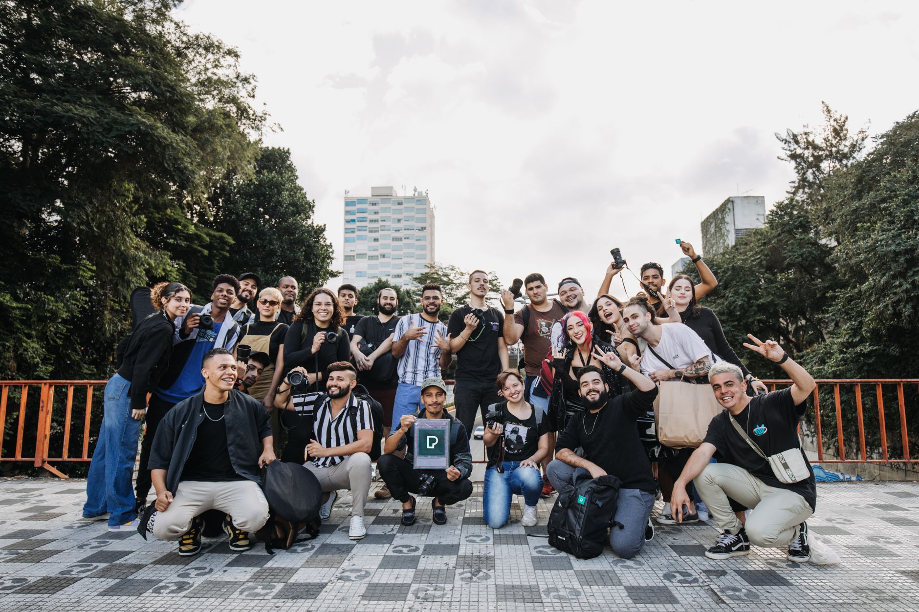 A large and diverse group of adults joyfully posing in an outdoor urban setting, celebrating unity.