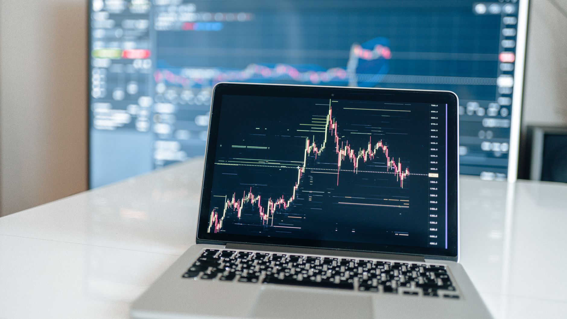 Laptop displaying cryptocurrency trading chart on a white desk.