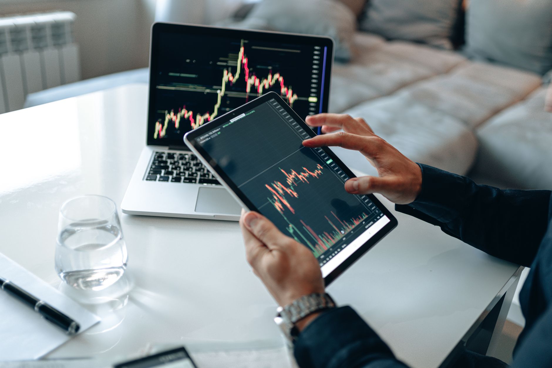 Trader analyzing stock market data on tablet with laptop in background.