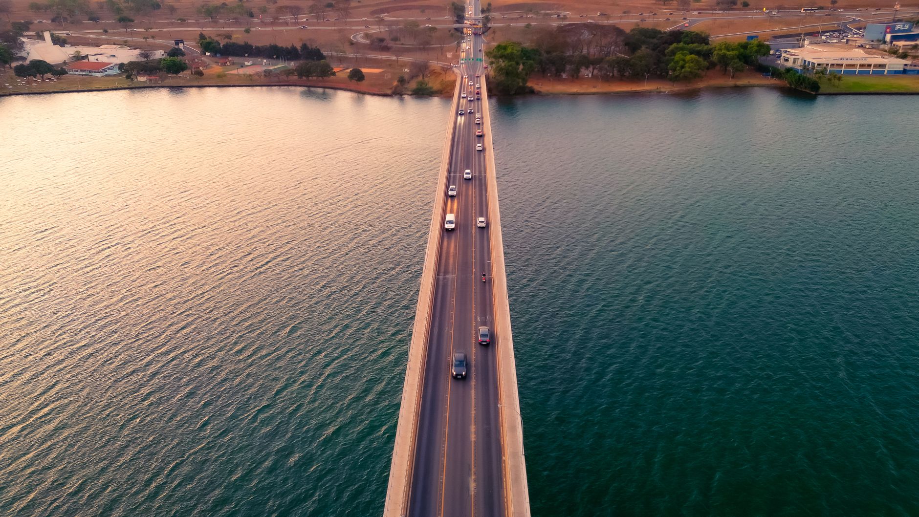 A stunning aerial view of JK Bridge over Lake Paranoá in Brasília during sunset, with cars in motion.