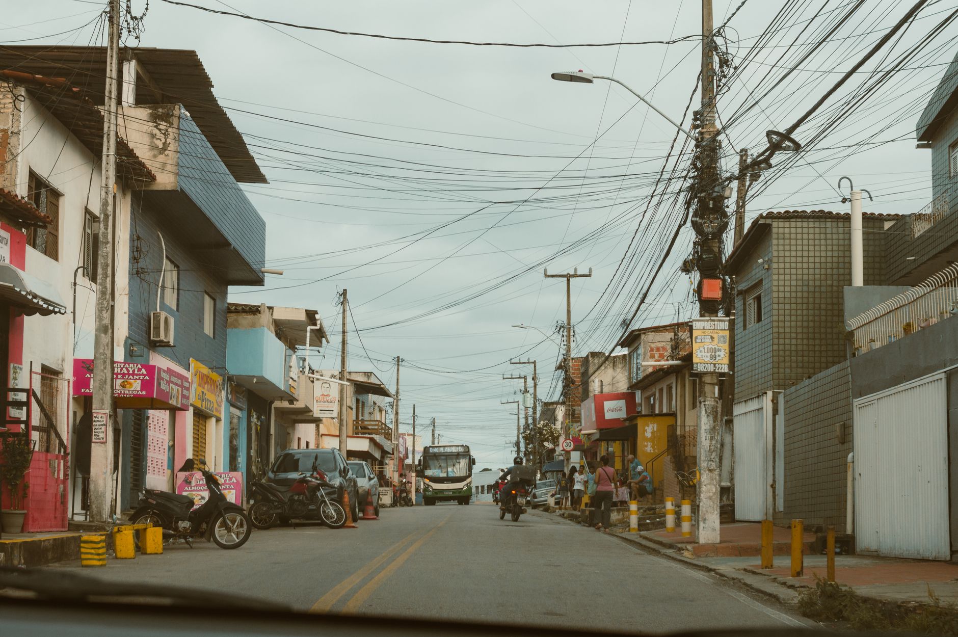 Vibrant street in RN, Brasil showcasing local shops and busy traffic on a cloudy day.