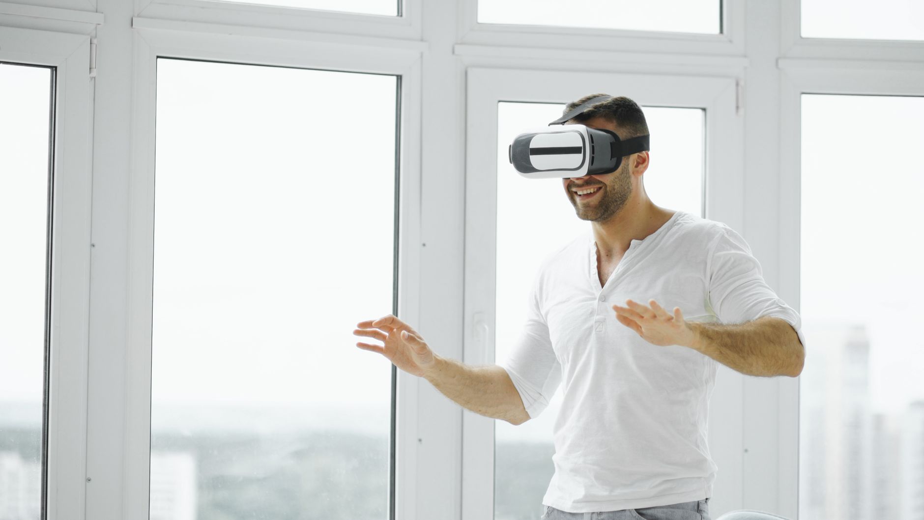 A joyful adult male enjoying virtual reality with VR headset in a bright indoor setting.