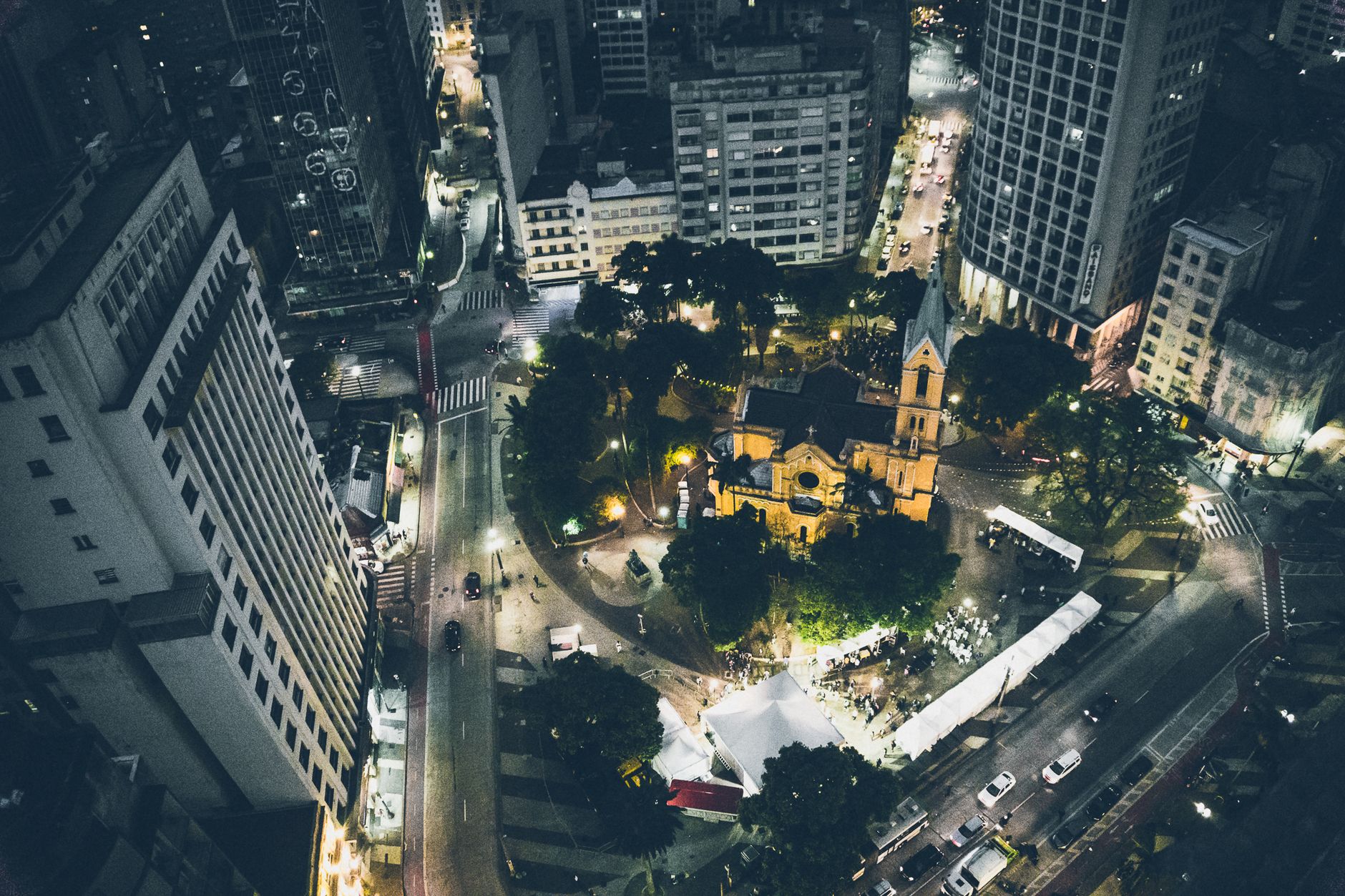 Aerial shot of a vibrant cityscape at night with an illuminated church and bustling streets.