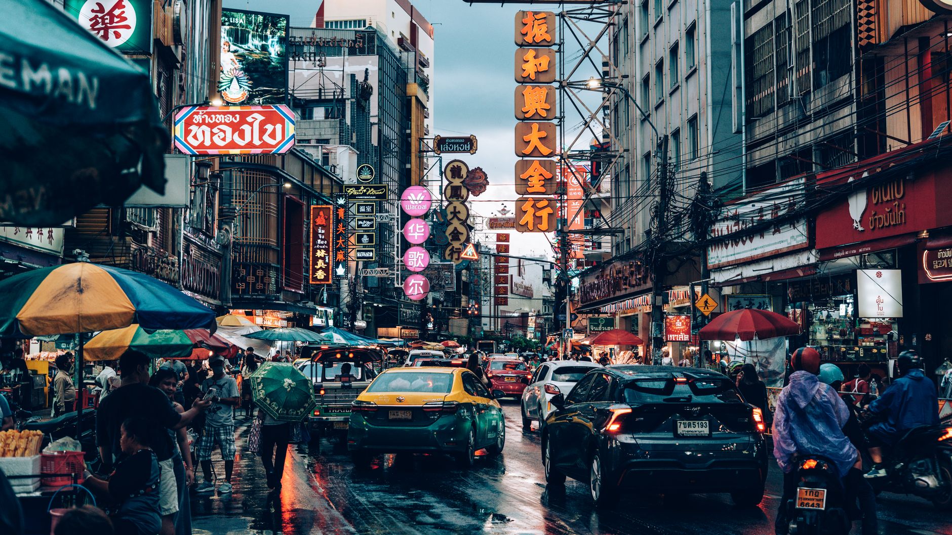 Bustling night market street scene in Bangkok, Thailand with neon signs and traffic.