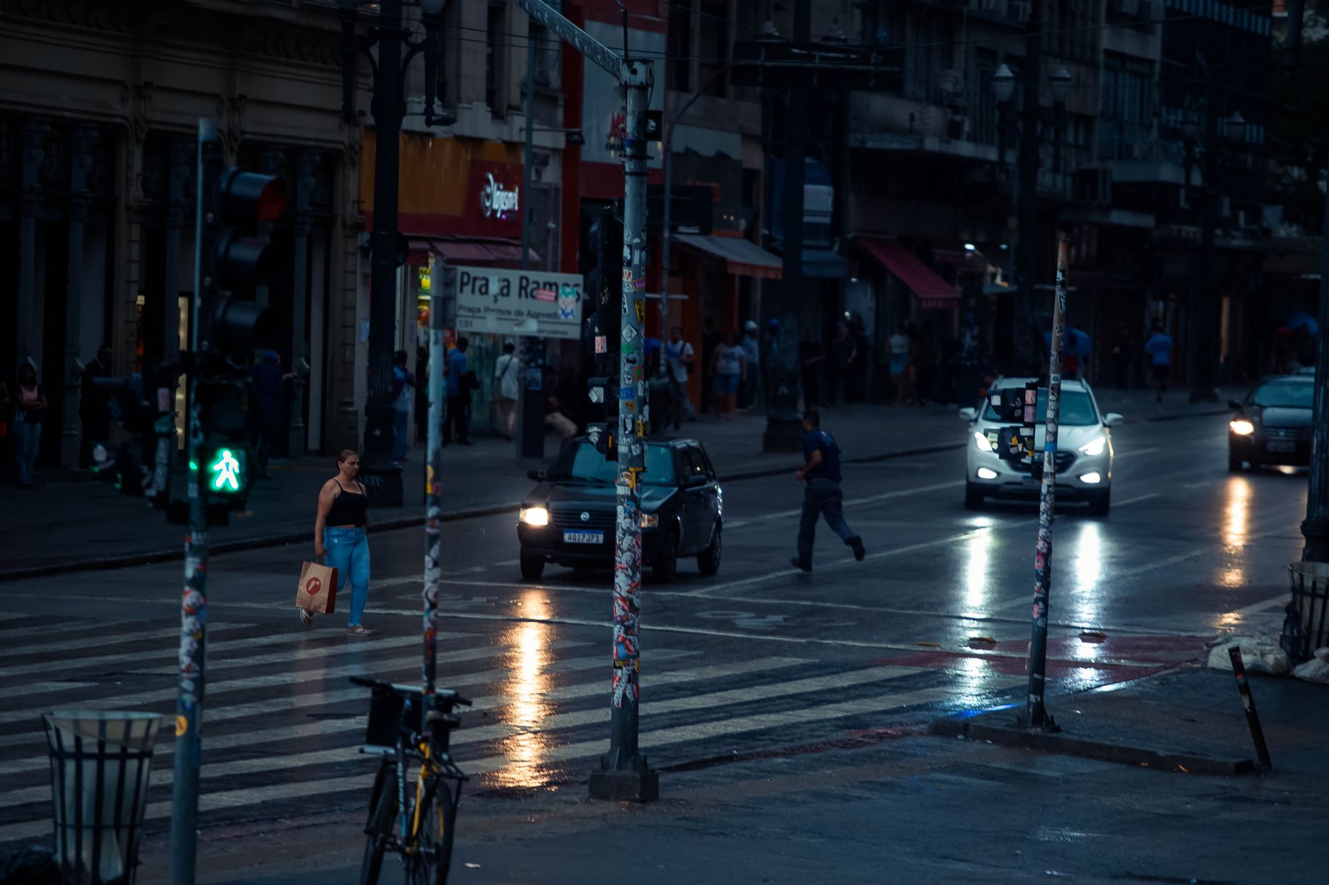 A moody street scene at dusk with cars and a pedestrian crossing in an urban environment.