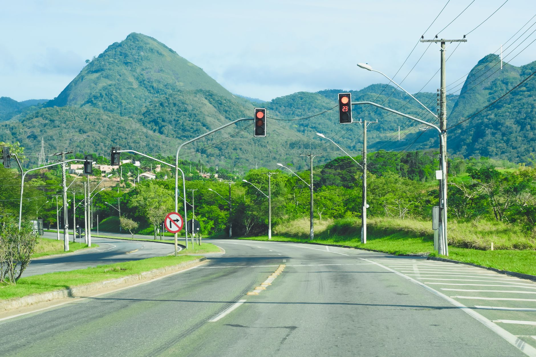 A curving highway with traffic lights amid lush greenery and mountain backdrop.