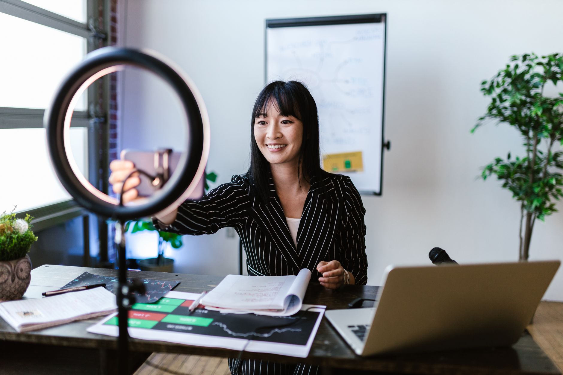 A woman vlogger uses her smartphone to create content in a professional office setting.