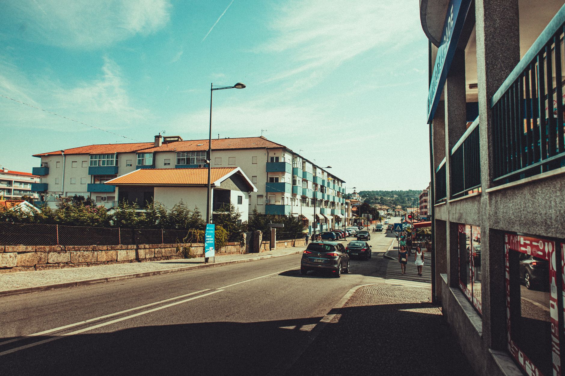 View of a sunny street with buildings and parked cars, typical of a Mediterranean town.