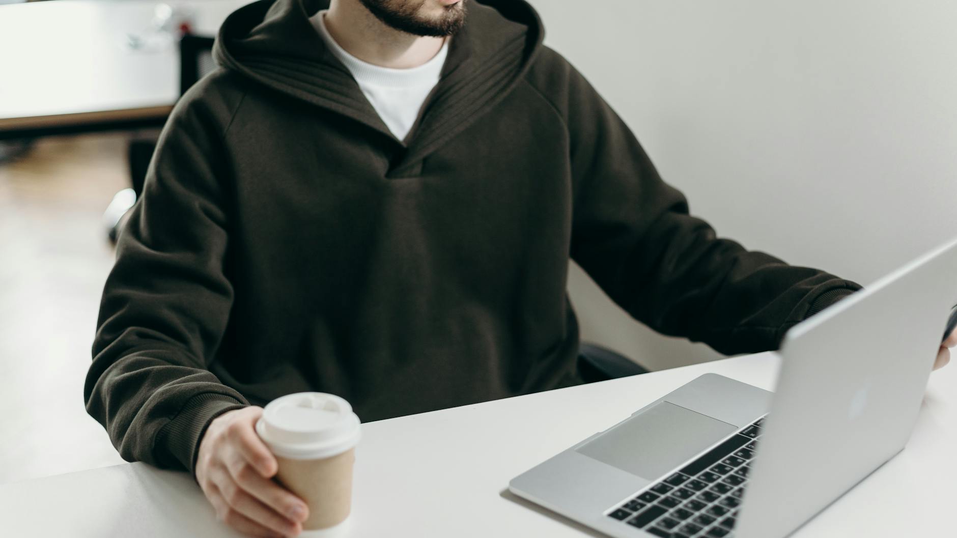 Young man working in a home office with laptop and coffee, embodying a casual work-from-home lifestyle.
