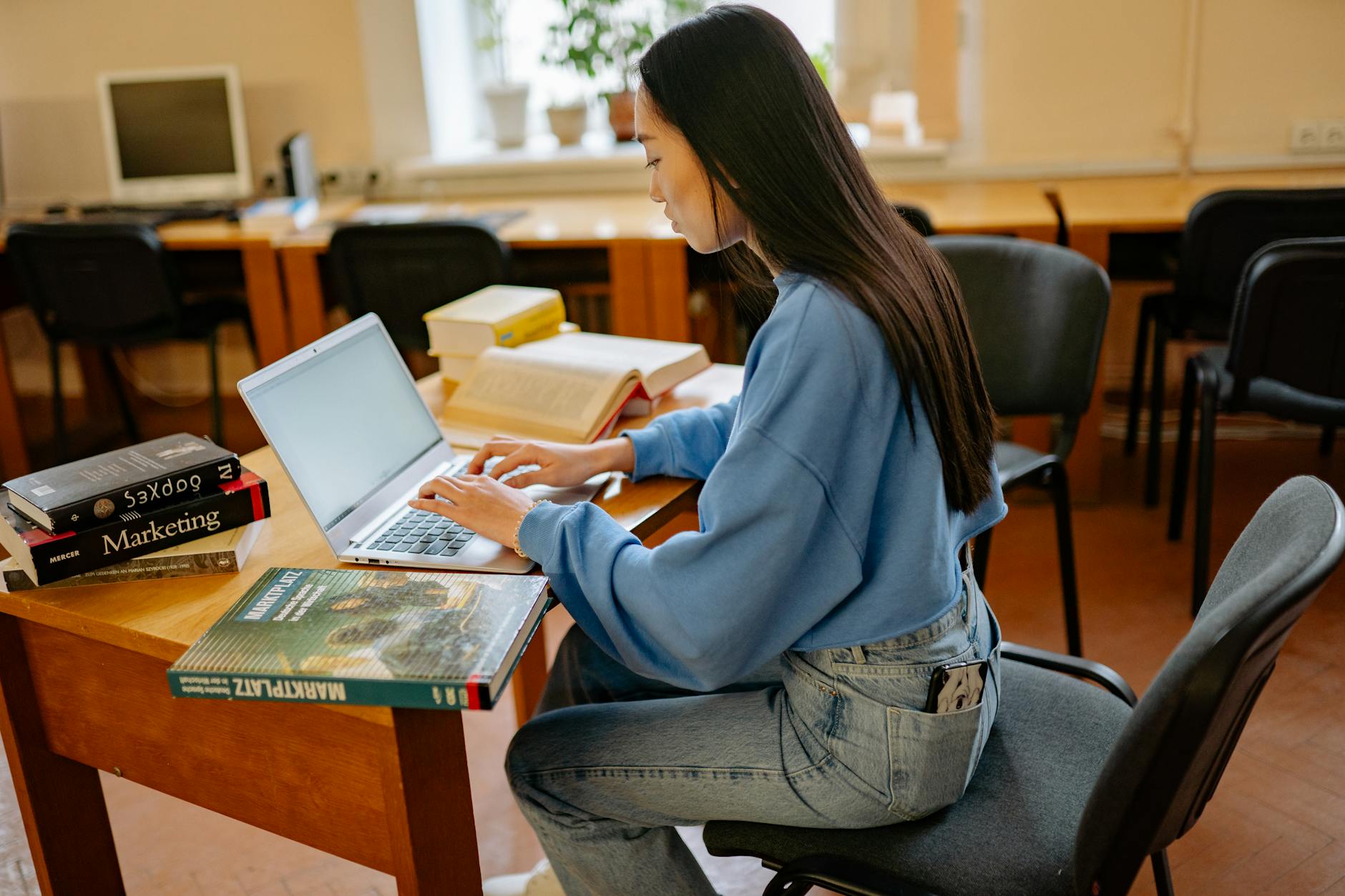 Focused woman typing on laptop, surrounded by books in a cozy study spot.