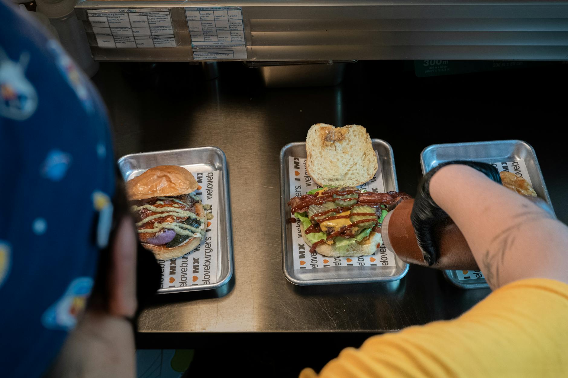 Chef in action preparing gourmet burgers with toppings in a restaurant kitchen setting.