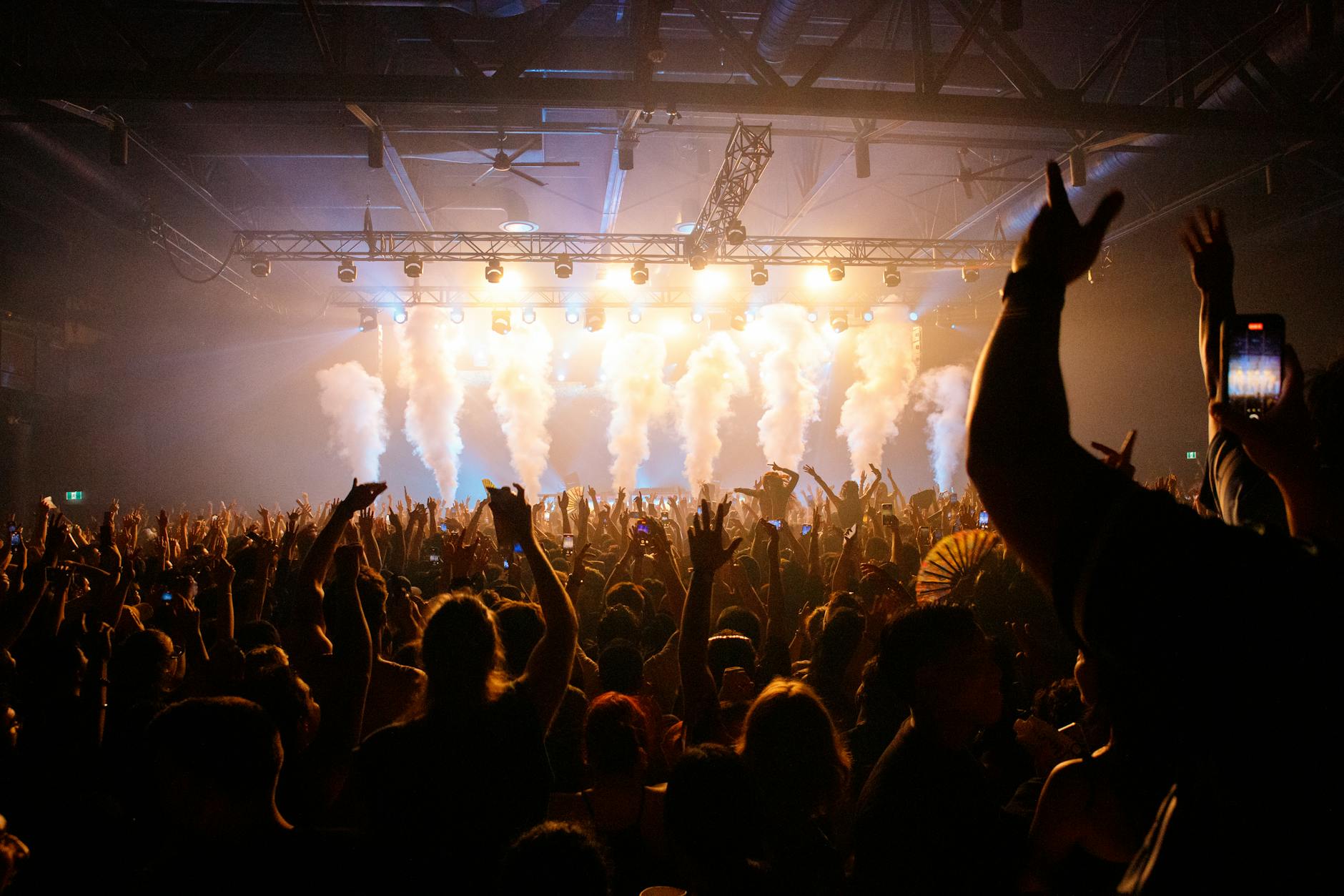 Energetic crowd enjoying a concert with dynamic lighting and smoke effects in an indoor venue.