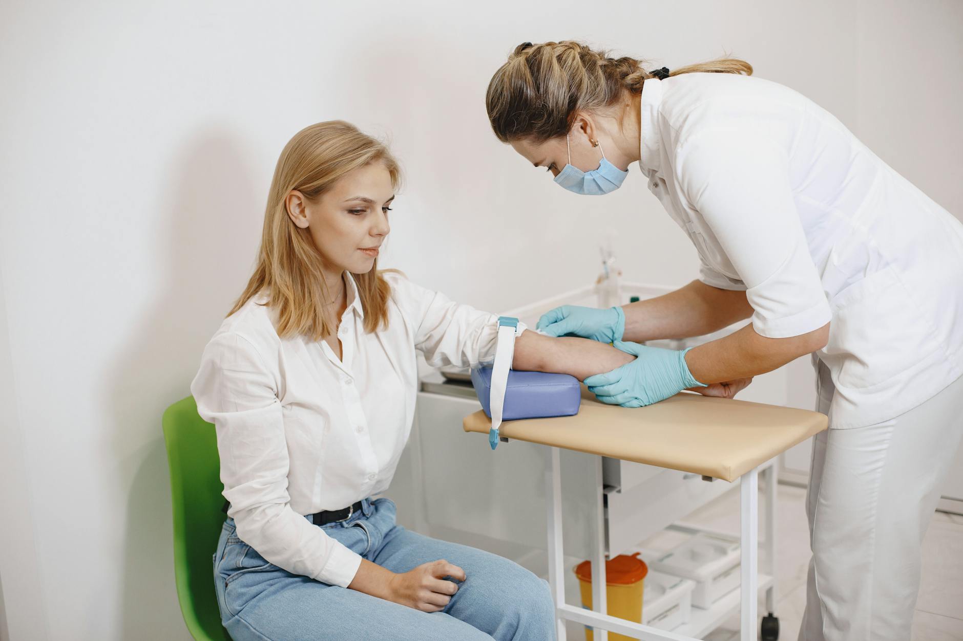 A nurse performs a blood test on a seated female patient in a medical setting.
