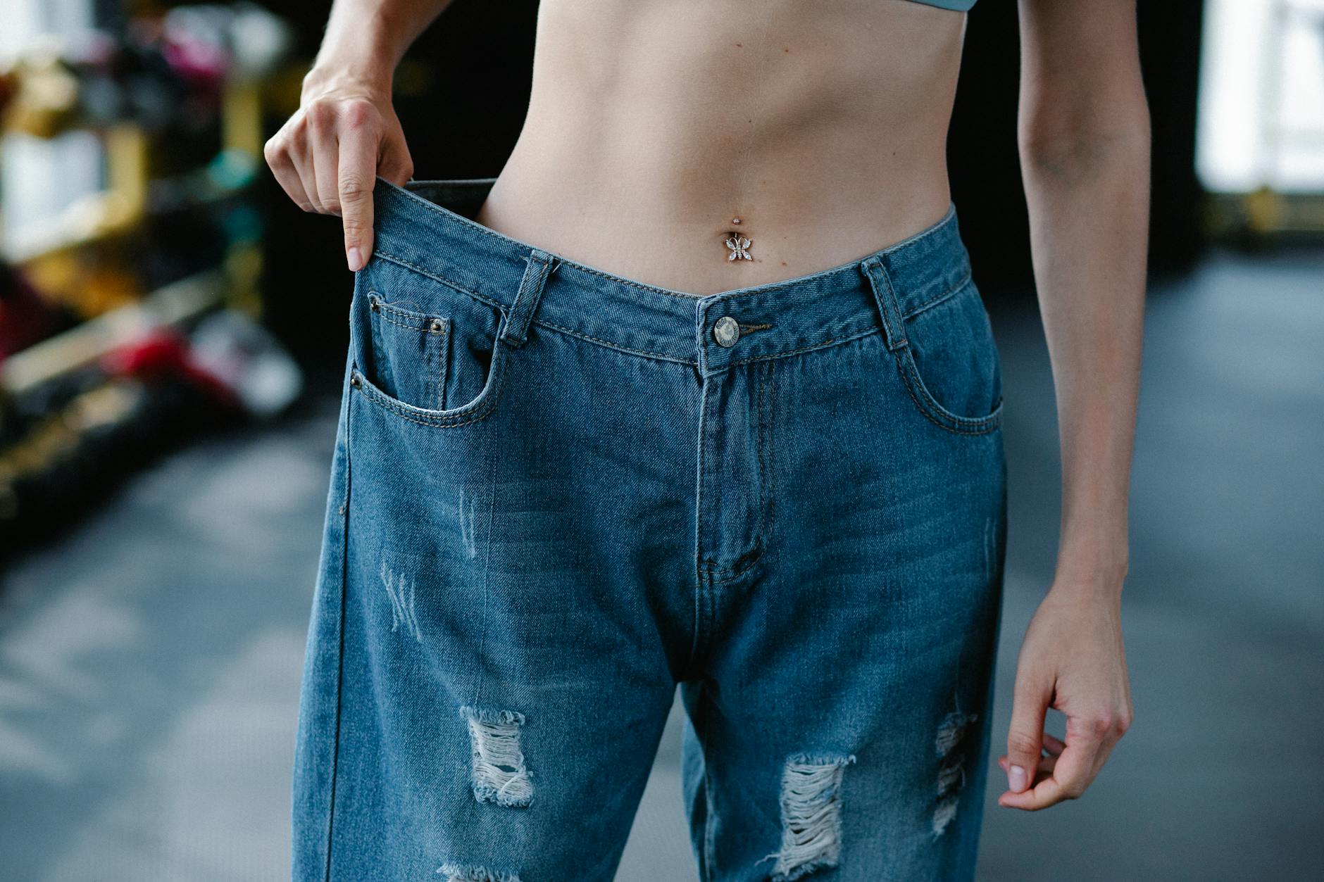 A woman showcases significant weight loss results confidently wearing loose jeans.