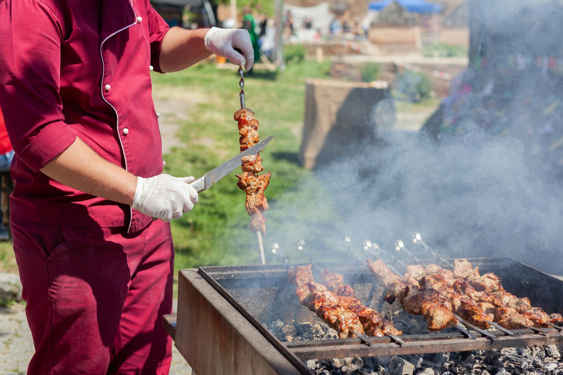 Chef grilling meat outdoors, slicing skewered kebabs over a charcoal grill, producing delicious smoky flavor.