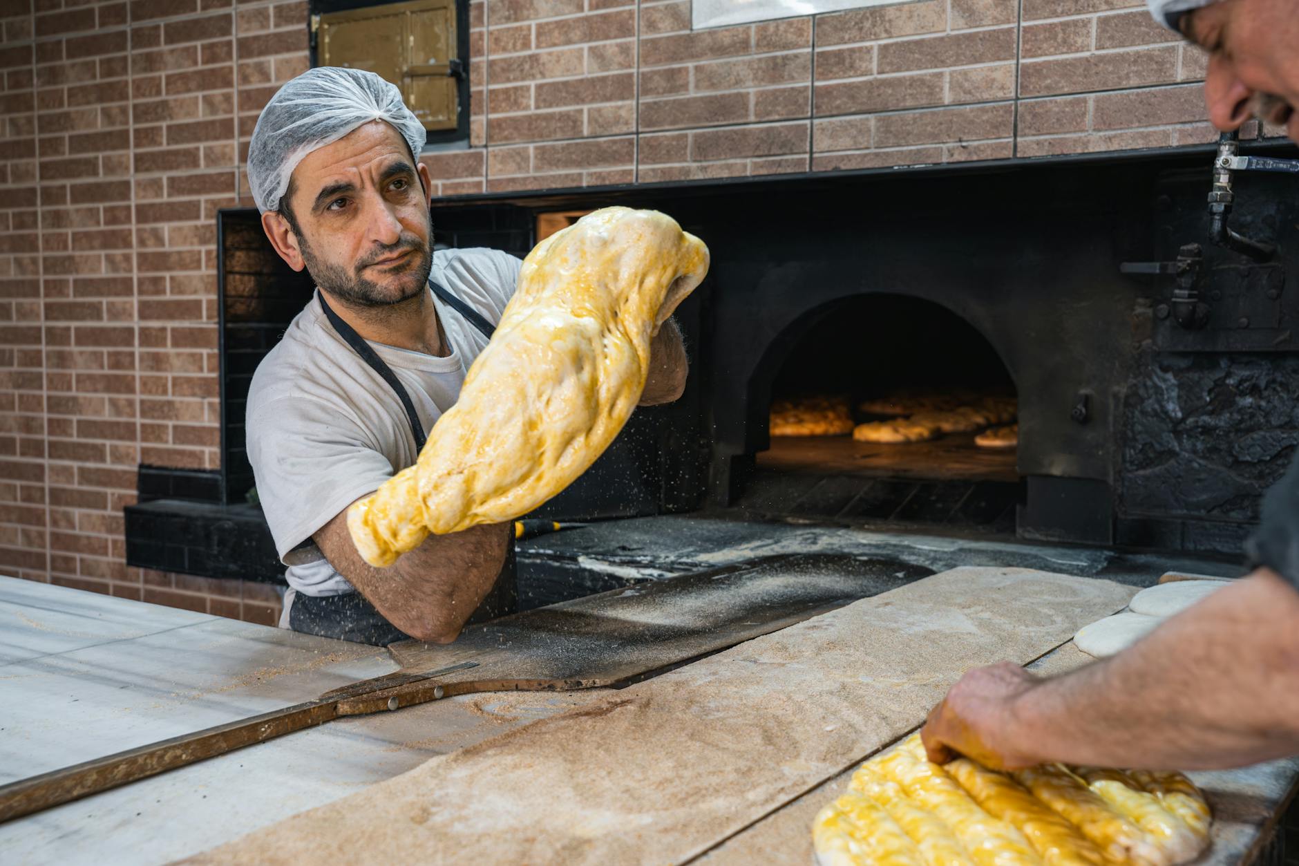 A baker skillfully handles dough in a brick oven bakery, making traditional flatbreads.