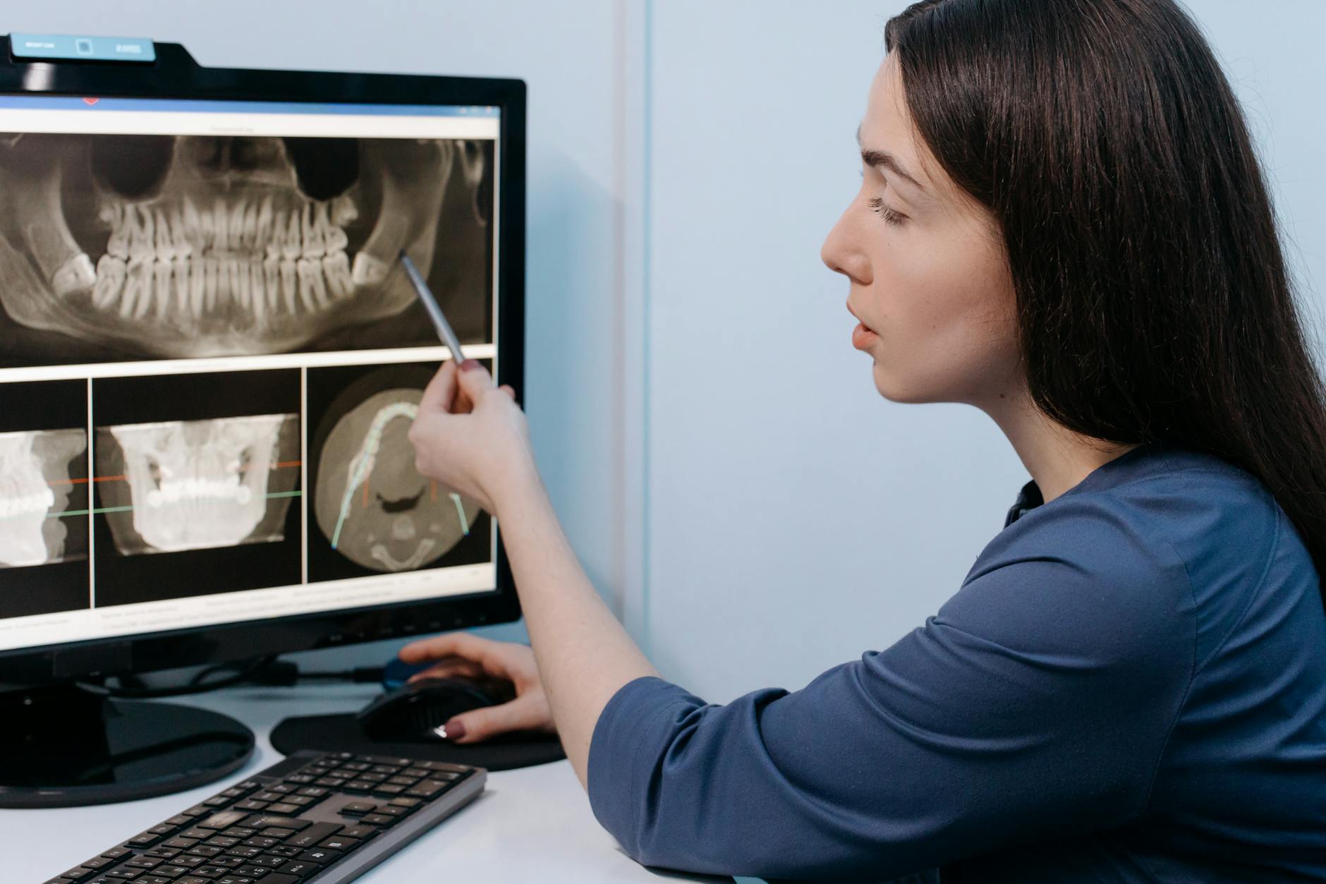 Female dentist examining dental X-ray images on computer screen in clinic.