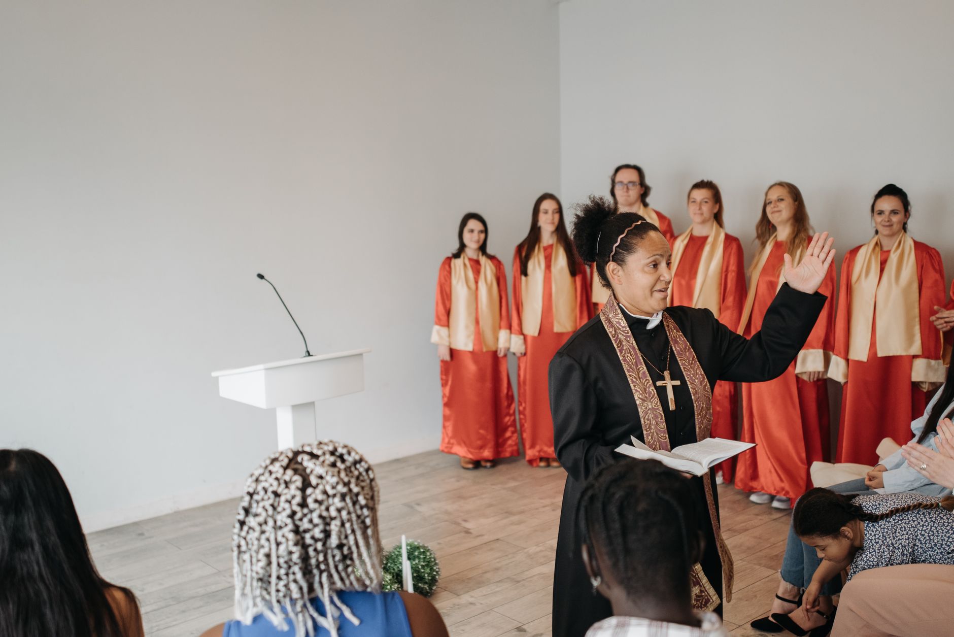 A pastor leading a church ceremony with a choir in red robes in the background.