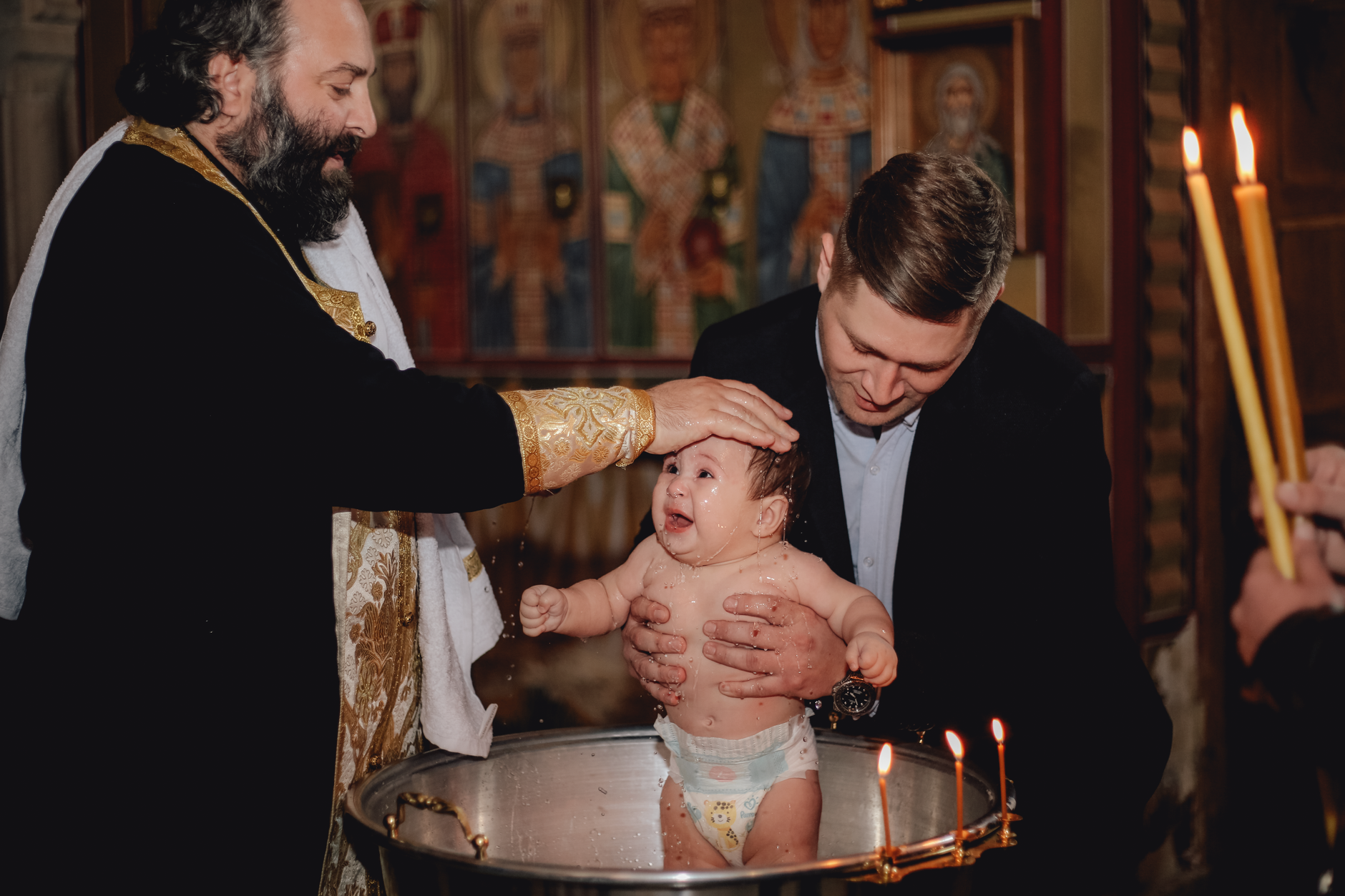 A priest performs a traditional baptism, blessing a baby in a church setting.