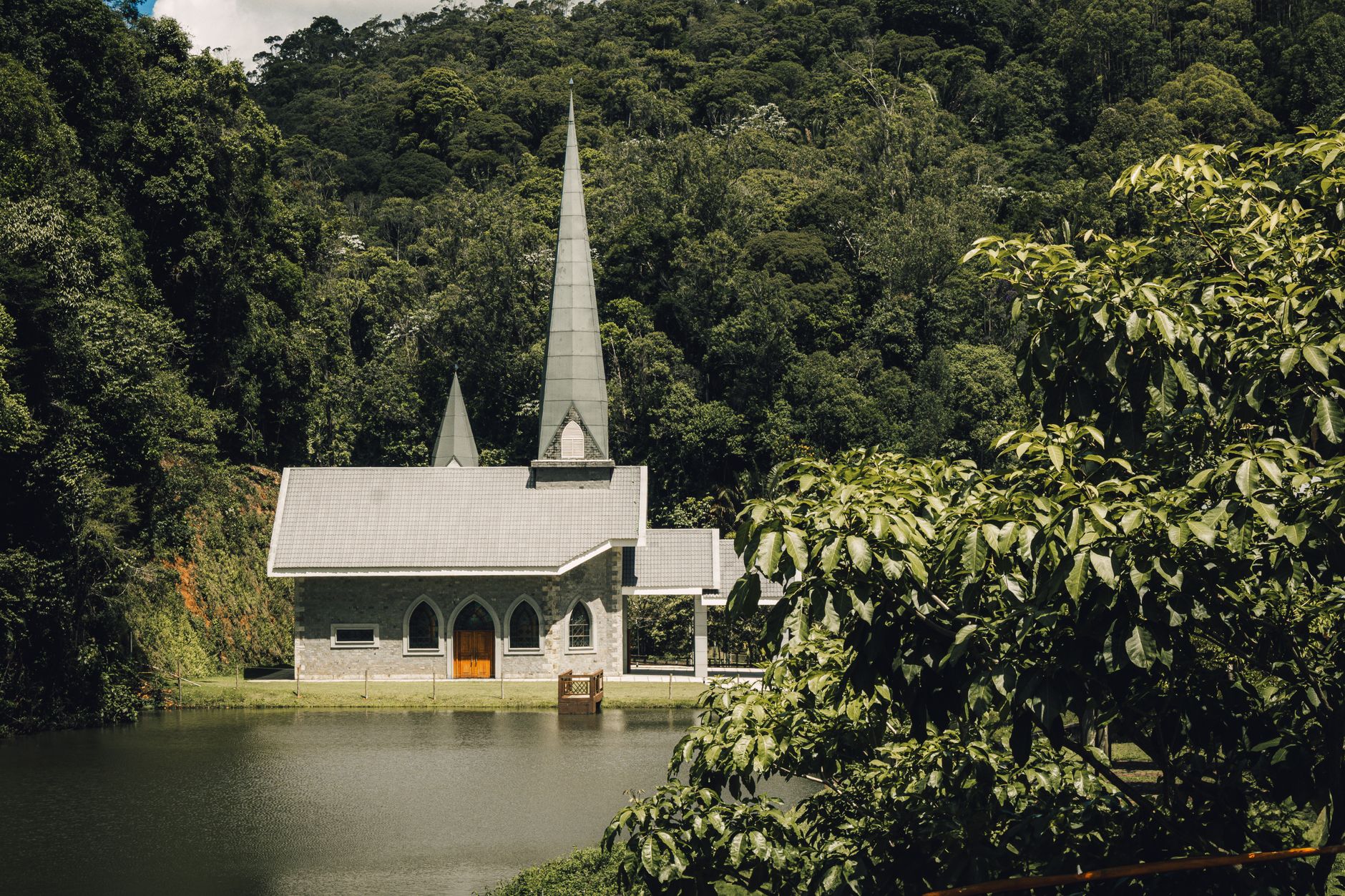 A charming stone church surrounded by lush forest near a serene lake.