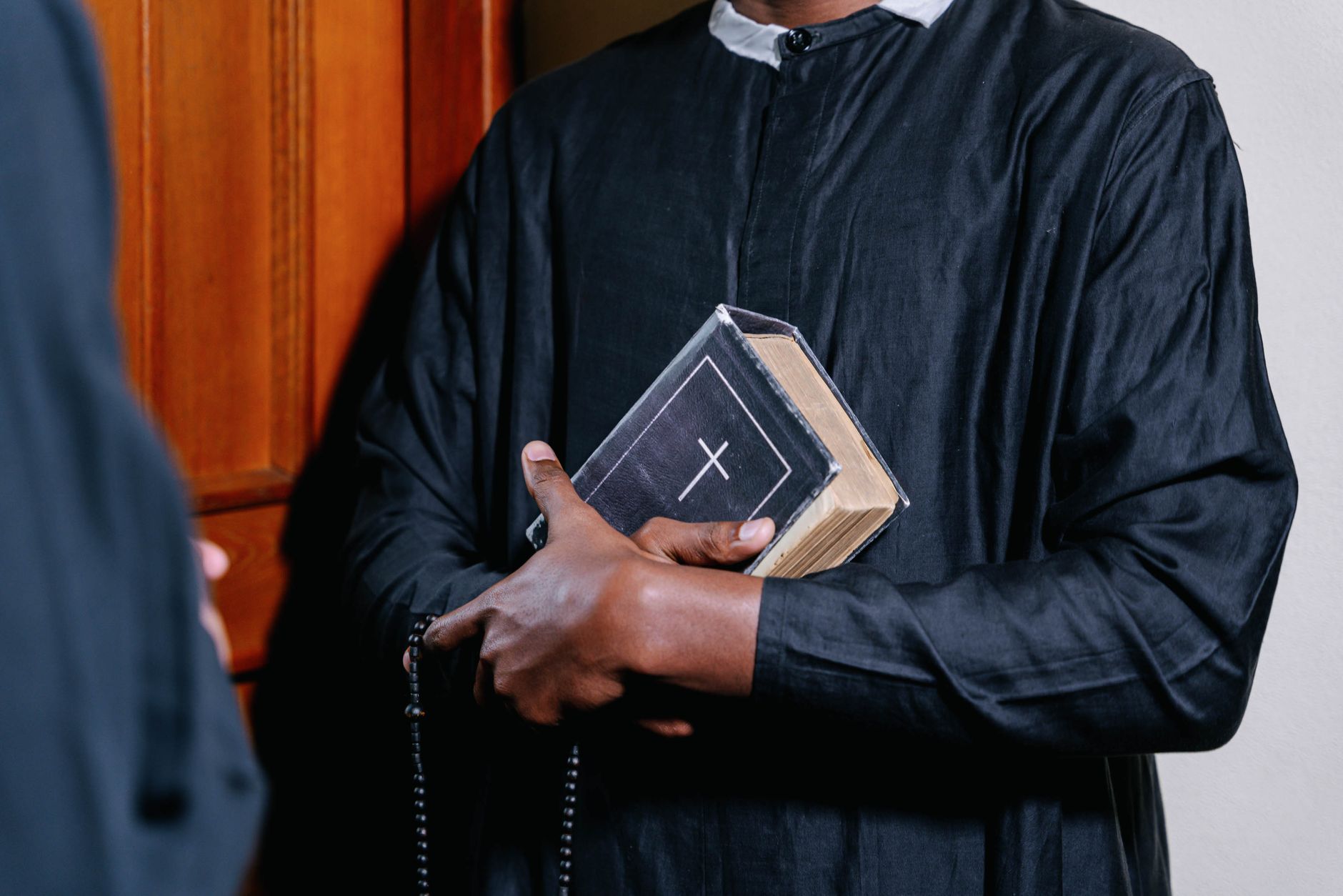 Close-up of a priest holding a Bible and rosary beads, symbolizing faith and spirituality.