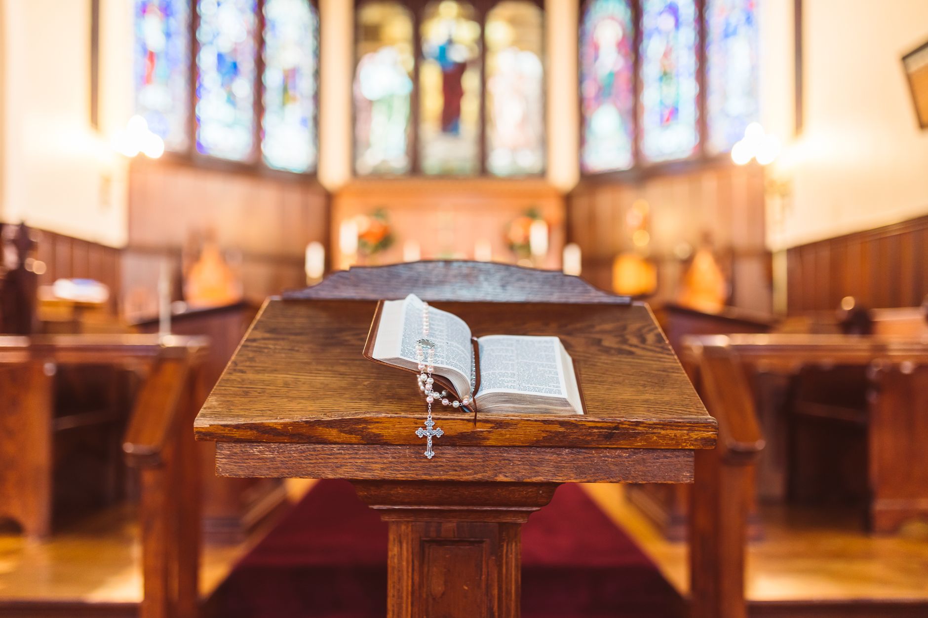 A wooden podium with an open Bible and rosary in a serene church setting.