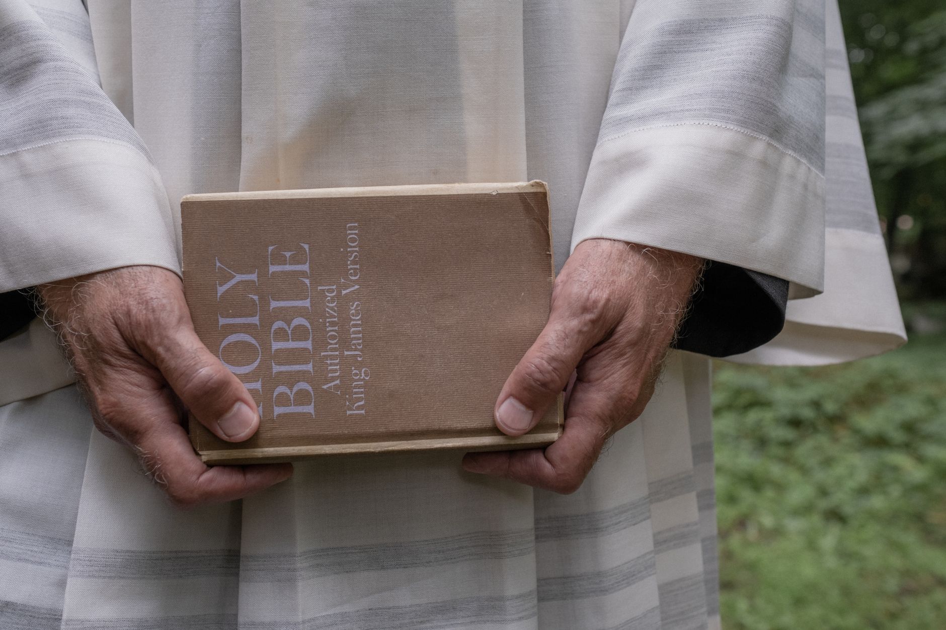 Close-up of a cleric holding a Holy Bible outdoors. Spiritual and religious theme.