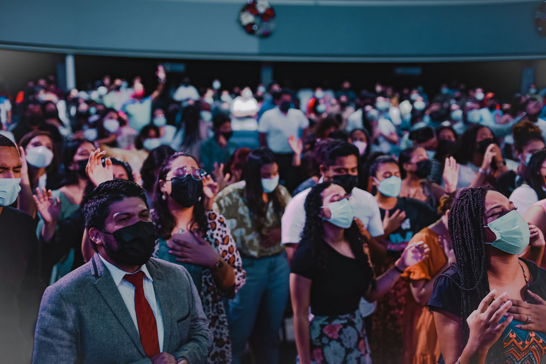 A large group of people gathered indoors for a religious ceremony, wearing face masks.